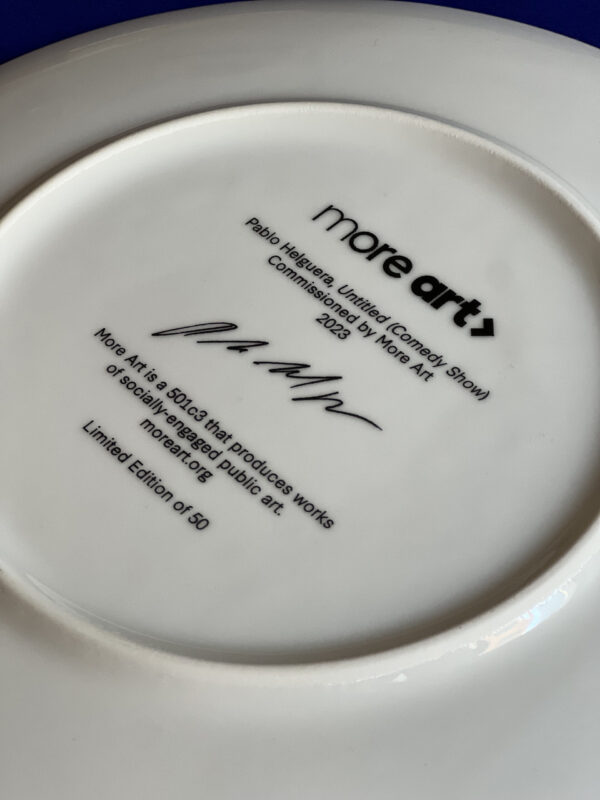 A photo of the back of a white porcelain plate. The More Art logo is printed on the plate back with a signature and other text